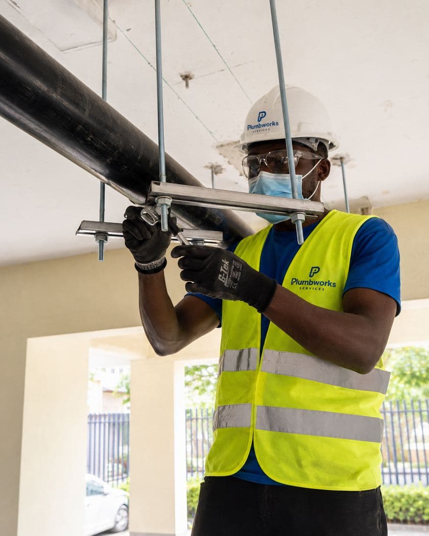 Plumbworks Abuja technician installing supported pipework in branded safety gear
